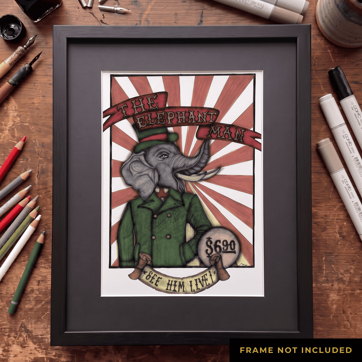 The Elephant Man print framed in black on the worktable, ink pens and pencils alongside