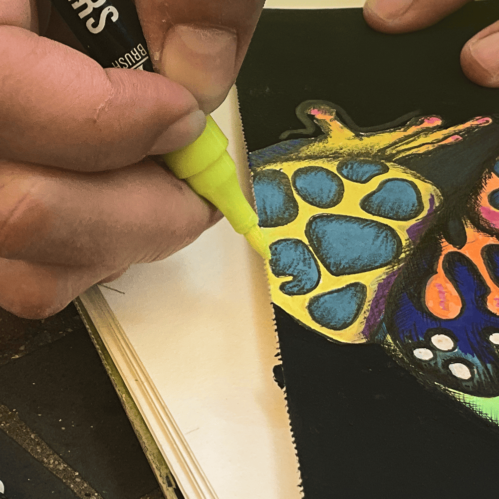 A yellow acrylic marker laid over the Psychedelic Frog's leg on black paper