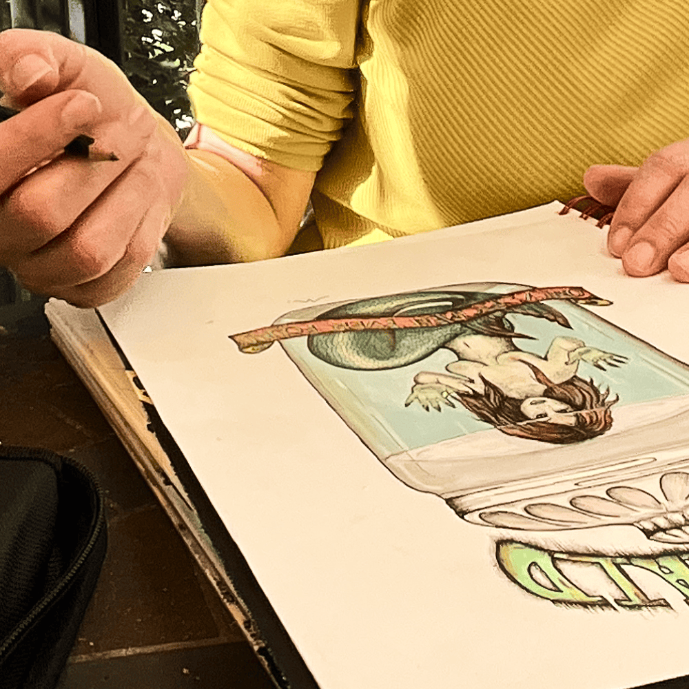 Maria Keller drawing the Fiji Mermaid by hand in a spiral-bound sketchbook